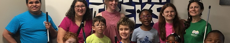 A group of kids and teachers from the 2018 NFB BELL Academy smiles at a rock climbing facility.
