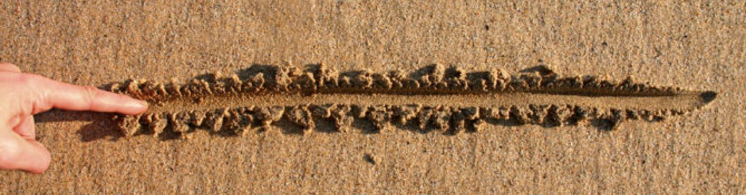 A finger draws a line from right to left in the tan sand.