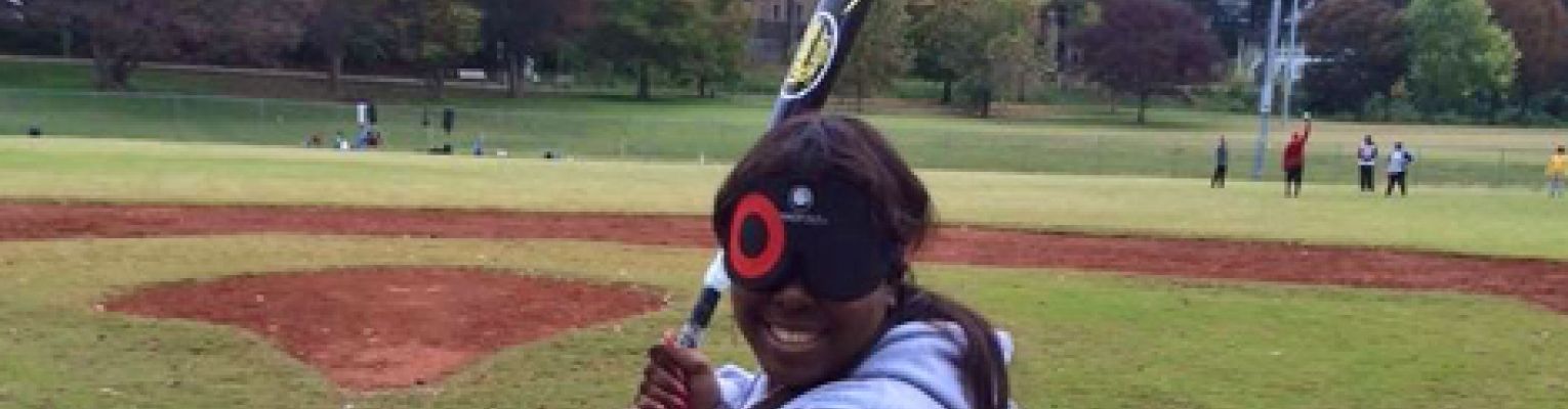 LaKeisha holds a bat and is standing in a baseball field.