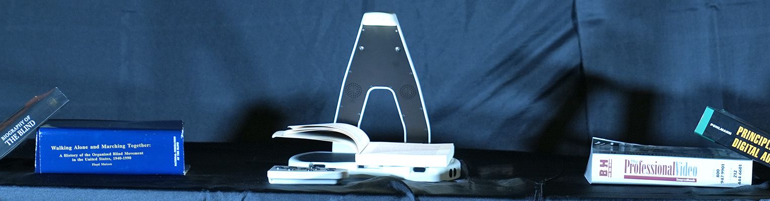 The Lyric Assistive Reader sits in the center of a table with books on either side.