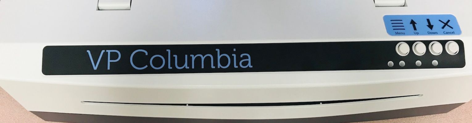 The ViewPlus Columbia Embosser rests on a table; the machine says "VP Columbia" and it has four buttons on the right front side.