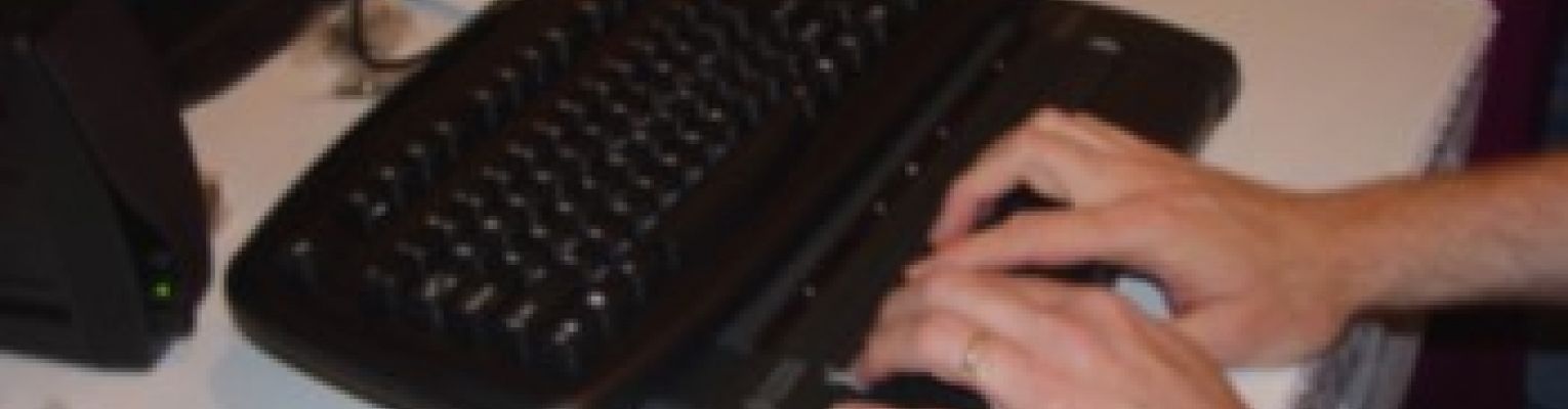 A person's hands rest on a Braille display in front of a computer.