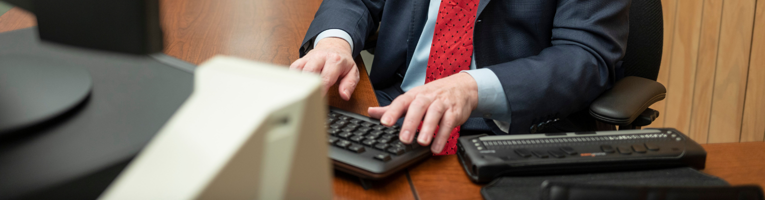 Person in a suit uses a QWERTY keyboard at a desktop computer