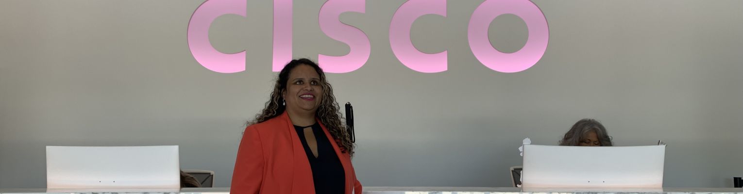 Mary Fernandez stands in front of a counter and a large CISCO sign.
